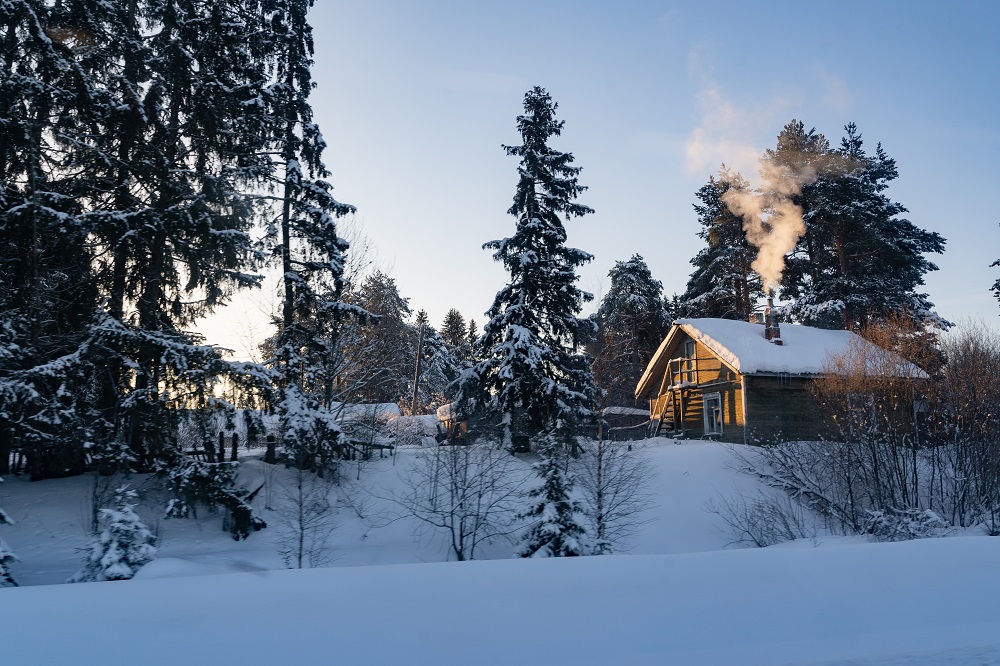 Dom w śnieżnym, zimowym krajobrazie, z dymiącym kominem